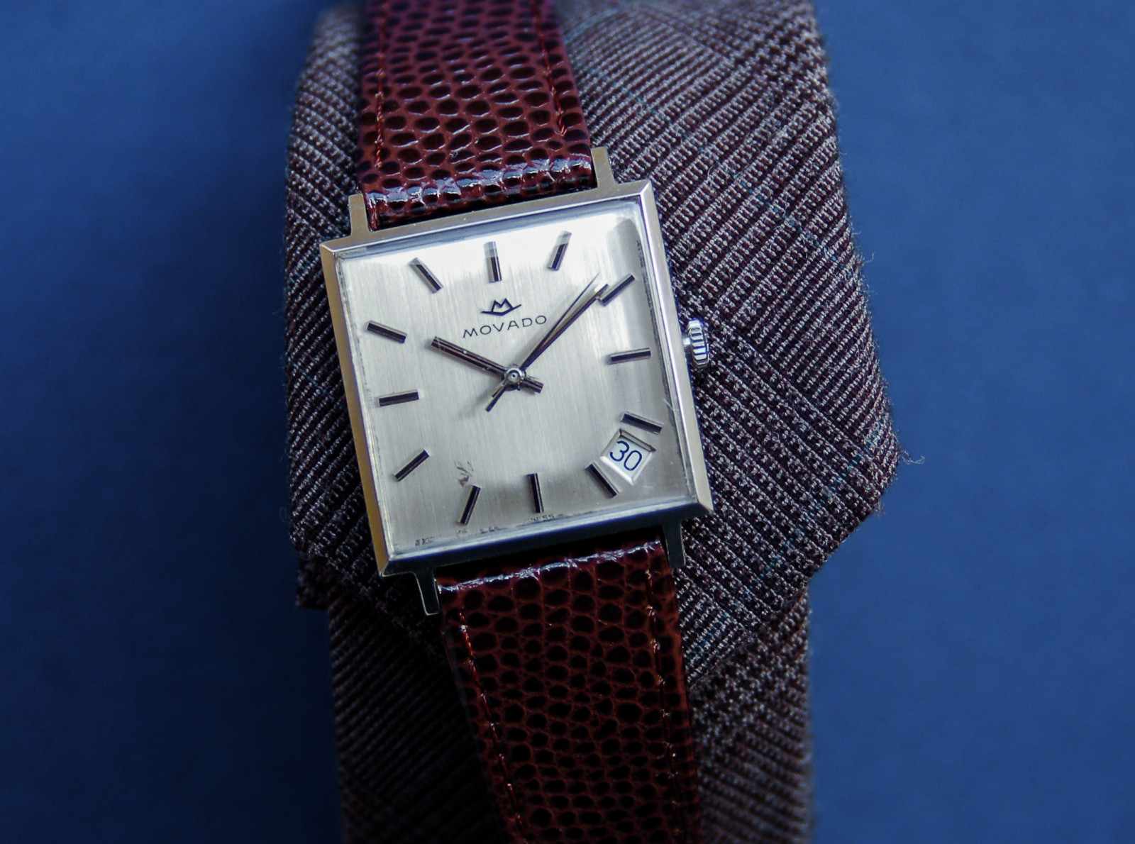 Sự khác biệt về giá giữa đồng hồ Movado mặt vuông dây kim loại và dây da.