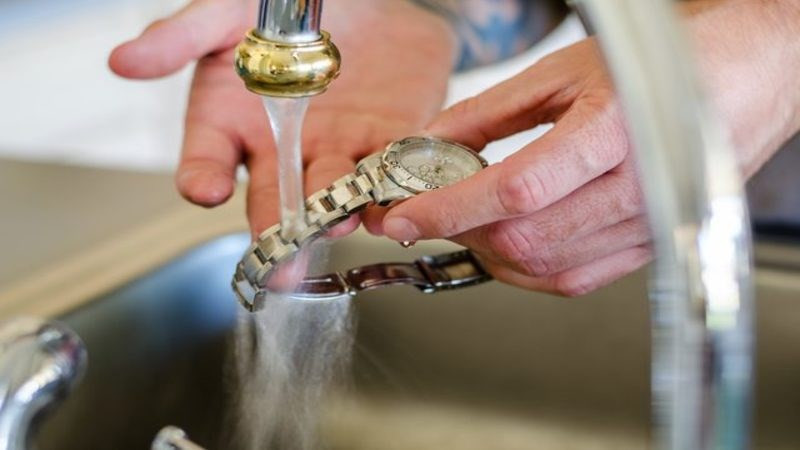 Rửa dây đồng hồ kim loại dưới vòi nước chảy nhẹ nhàng để loại bỏ bụi bẩn thông thường.